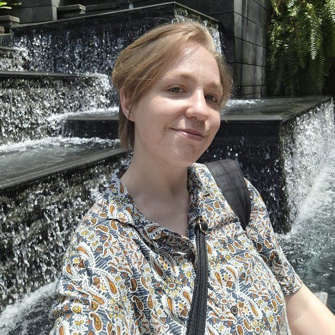 photograph of mol, a white person with blonde hair wearing patterned shirt, smiles at the camera